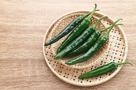 Green chili served in bamboo plate on wooden table.