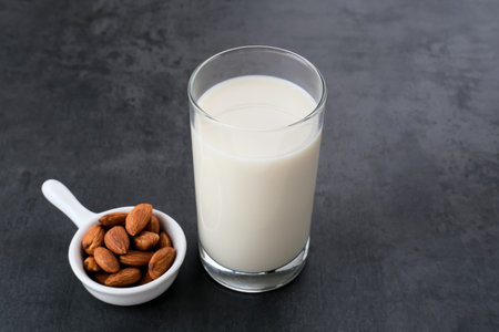 Almond milk in glass with almonds on dark background. Space for text