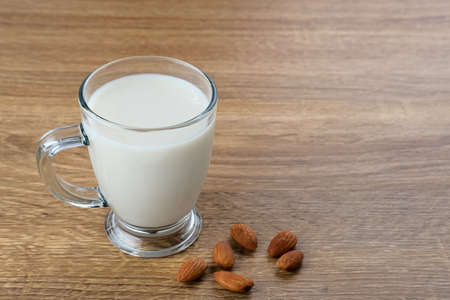 Almond milk in glass with almonds on wooden table. Space for textの写真素材