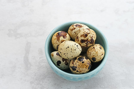 Fresh Quail Eggs served in bowl on grey background. Space for text