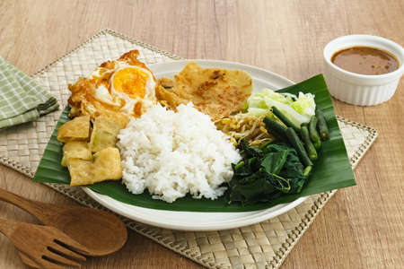 Nasi Pecel, a traditional Javanese rice with vegetable salad and peanut sauce, served with side dishes such as egg, martabak, and peyek crackers.の写真素材