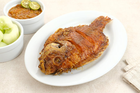 Grilled Tilapia with honey and soy sauce or Ikan Nila Bakar. Served on white plate with sambal (chilli sauce) and cucumberの写真素材