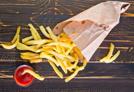 Potatoes fries in a little white paper bag on tomato sauce in bowlの写真素材