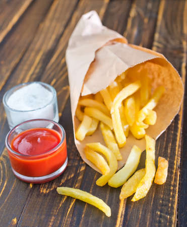 Potatoes fries in a little white paper bag on tomato sauce in bowlの写真素材