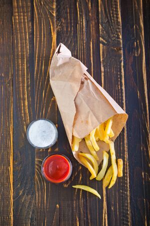 Potatoes fries in a little white paper bag on tomato sauce in bowlの写真素材