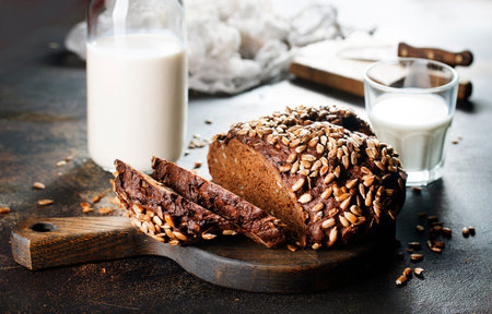 Homemade rustic rye bread with sunflower seeds and a bottle of milk on old tableの写真素材