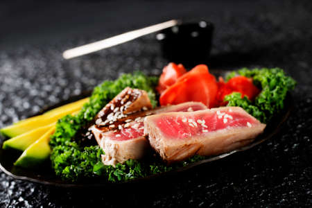 Grilled Tuna Steak and Avocado on a black plateの写真素材