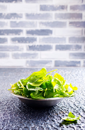 Fresh baby spinach leaves in bowl on stone backgroundの写真素材