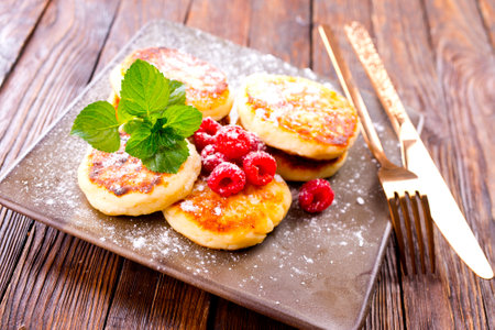 Traditional sweet syrniki or cottage cheese pancakes served with sweet cream and fresh raspberries in a white plate over table.の写真素材