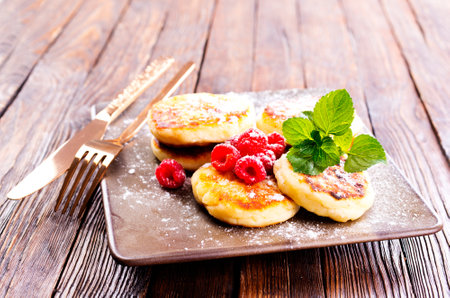 Traditional sweet syrniki or cottage cheese pancakes served with sweet cream and fresh raspberries in a white plate over table.の写真素材