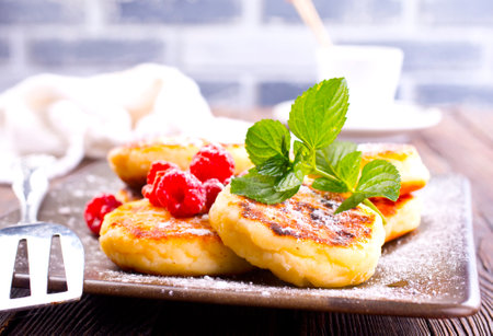 Traditional sweet syrniki or cottage cheese pancakes served with sweet cream and fresh raspberries in a white plate over table.の写真素材