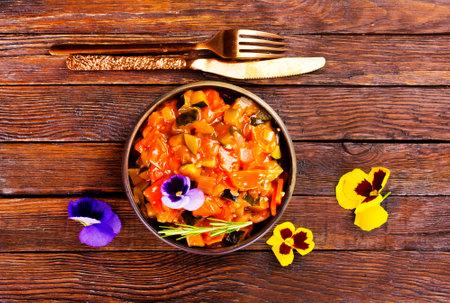 vegetable stew, eggplant, onion, zucchini with tomato sauce, garlic and herbs in a baking dish on a wooden table, landscape view from above, close-up, flat lay, free spaceの写真素材