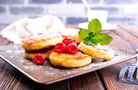 Traditional sweet syrniki or cottage cheese pancakes served with sweet cream and fresh raspberries in a white plate over table.の写真素材