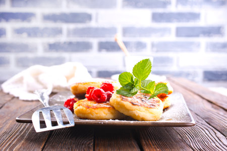 Traditional sweet syrniki or cottage cheese pancakes served with sweet cream and fresh raspberries in a white plate over table.の写真素材