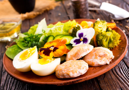 salmon cutlets on a plate with vegetables and boiled eggsの写真素材