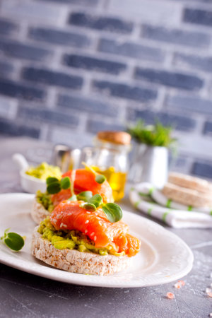 diet sandwiches with rye bread, avocado, smoked salmon on a white plateの写真素材