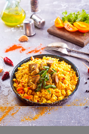 Pilaf, a dish of rice, chicken, carrots with spices and dried cranberries on a black plate on a table. Eastern cuisine.の写真素材