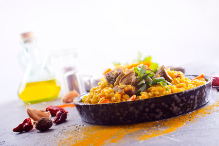 Pilaf, a dish of rice, chicken, carrots with spices and dried cranberries on a black plate on a table. Eastern cuisine.の写真素材