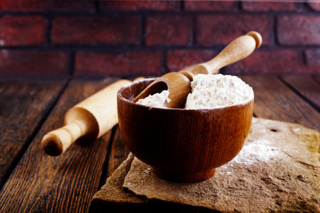Overhead view of bowl with flour placed on messy wooden table in kitchen of bakehouse during cooking processの写真素材