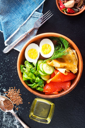 Delicious healthy brunch - boiled egg, smoked salmon, green salad and savory pancakes on a dark backgroundの写真素材