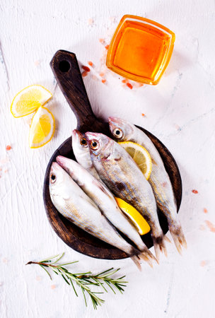 small fish with salt and spice on board on white tableの写真素材