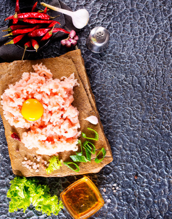 Raw minced meat in bowl on table and ingredients. Ground meat with ingredients for cooking on dark background with copy space.の写真素材