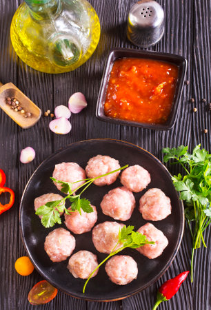 Fresh raw beef meatballs with spices and tomato sauce on dark backgroundの写真素材