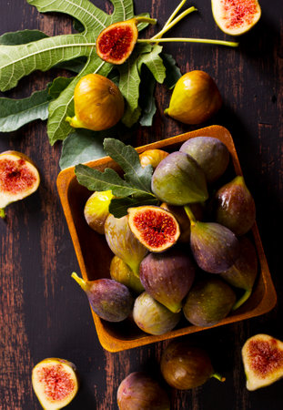 A wooden bowl filled with fresh, ripe figs sits on a rustic wooden table, with a few more figs scattered around.の写真素材