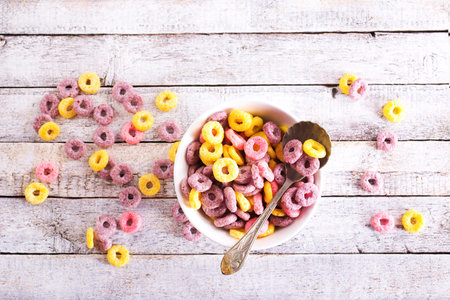 Bowl and plate of colorful cereal rings on light grunge background