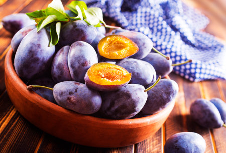 Fresh plums on plate on wooden tableの写真素材