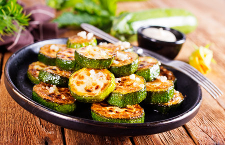 Tasty fried zucchini slices on a plate with sauce on a wooden table.の写真素材