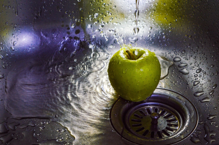 Green apple under the pressure of water in the kitchen sinkの写真素材