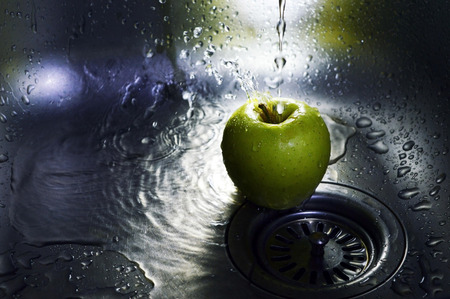 Green apple under the pressure of water in the kitchen sinkの写真素材