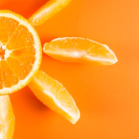 Orange slices spread around a cut half of an orange fruit on orange colored background