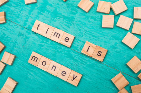 Time is money words laid out with wooden letters of the alphabet concept on a blue backgroundの写真素材