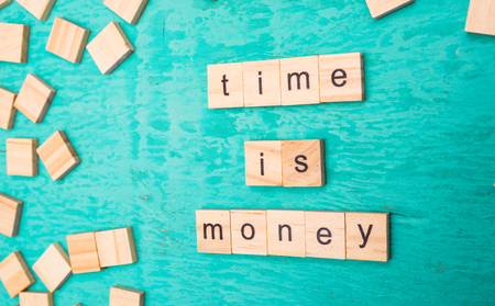 Time is money words laid out with wooden letters of the alphabet concept on a blue backgroundの写真素材