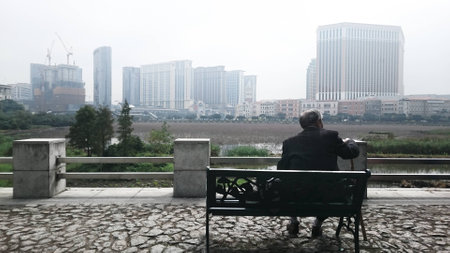 old man sitting on park bench and looking at the cityの写真素材