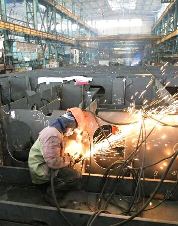 Welder welding a metal part in a dark industrial environment.の写真素材