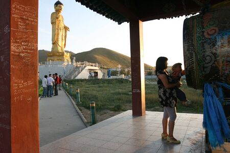 Woman take care a boy on her hand in front of Buddha statue, August 14, 2008. Ulan Bator . Mongoliaのeditorial素材