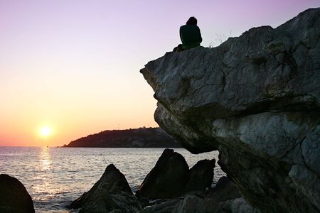 A young person sitting on a stone at sunset in Crimea, Ukraineの写真素材