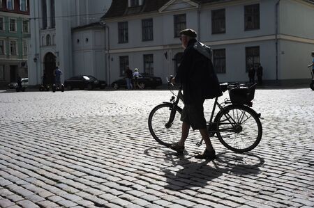 RIGA, LATVIA - AUGUST 9: Man walking his bicycle on an old cobblestone road in Old Town of Riga on August 9, 2010のeditorial素材