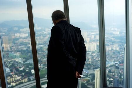 Kuala Lumpur, Malaysia - April 4, 2011: Businessman looking through the window of Petronas Twin Tower down to Kuala Lumpur city. Petronas Twin Towers  are skyscrapers and  the tallest twin buildings in the world.のeditorial素材
