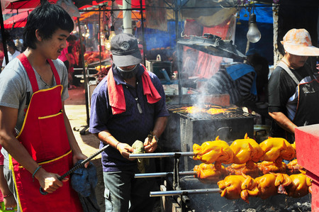 BANGKOK, THAILAND - FEB 23, 2013: Man cooking grilled chicken on the market in traditional Thailand way.のeditorial素材