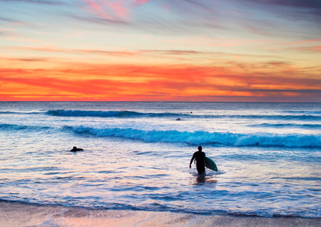 Surfer with surfboard walking out of the ocean at sunsetの写真素材