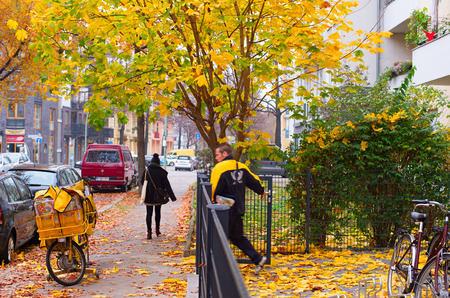 BERLIN, GERMANY - NOVEMBER 15, 2014: Typical German Postman with his delivery bike distributes mail. Deutsche Post DHL has 467,088 employees ( in more than 220 countries )のeditorial素材
