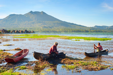 BALI ISLAND, INDONESIA - APRIL 26, 2013: Balinese fisherman in traditional boat in a caldera lake of Batur volcano, volcano on the background.  Batur is the most active volcano Bali and one of Indonesia's more active onesのeditorial素材