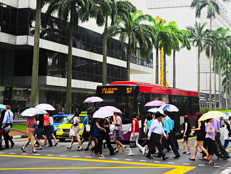 SINGAPORE - MARCH 06, 2013: People crossing the street in the rain in Singapore Downtown Core. There are more than 7,000 multinational corporations from US States, Japan and Europe in Singaporeのeditorial素材