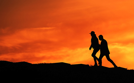 Man and woman walking on a hill at sunsetの写真素材
