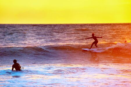Surfers surf in the ocean at sunset. Bali island, Indonesiaの写真素材