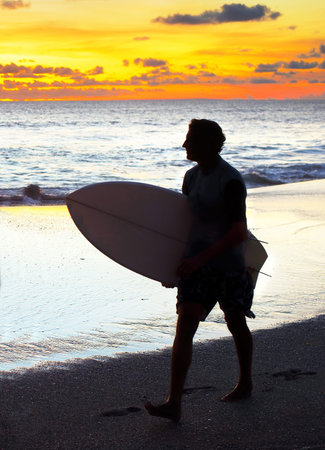 Surfer with surfboard walking on the ocean beach at sunset. Bali island, Indonesia